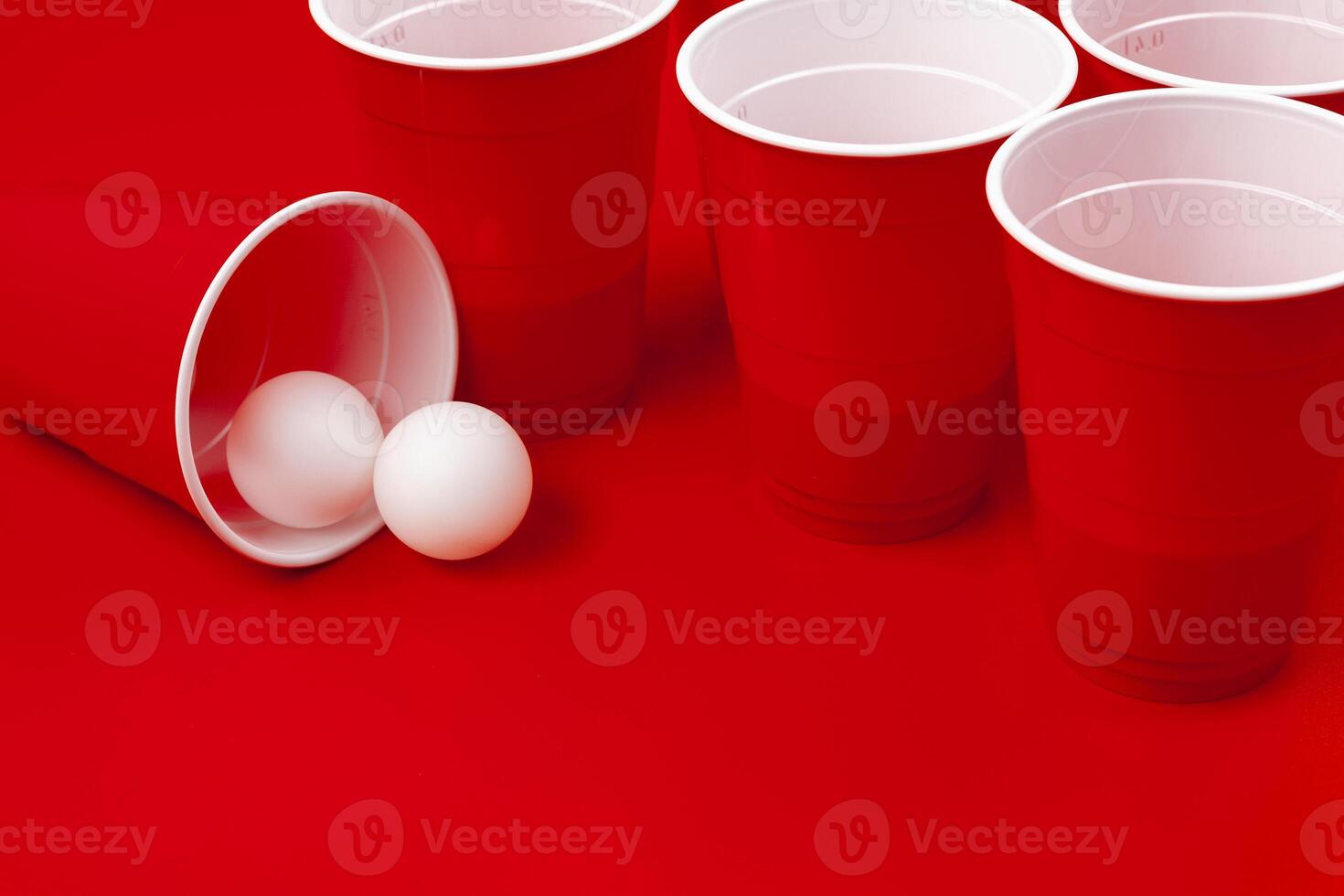 Cups and plastic ball on red background. Beer pong game photo