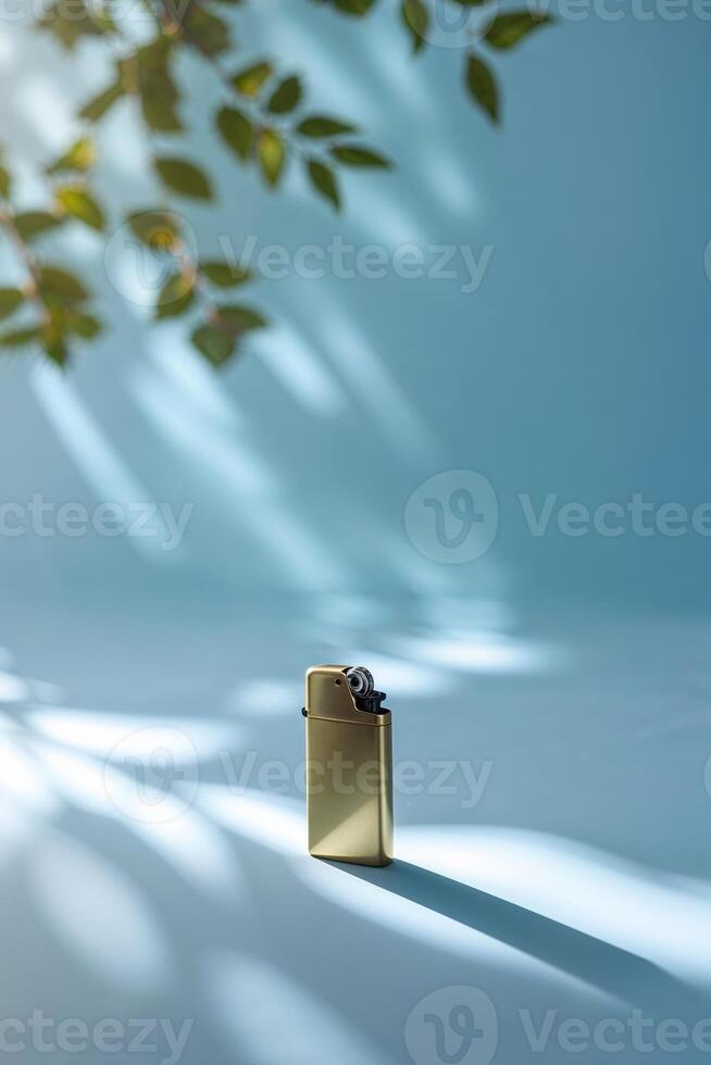Elegant golden lighter resting on a softly lit blue surface surrounded by natural shadows and leaves photo