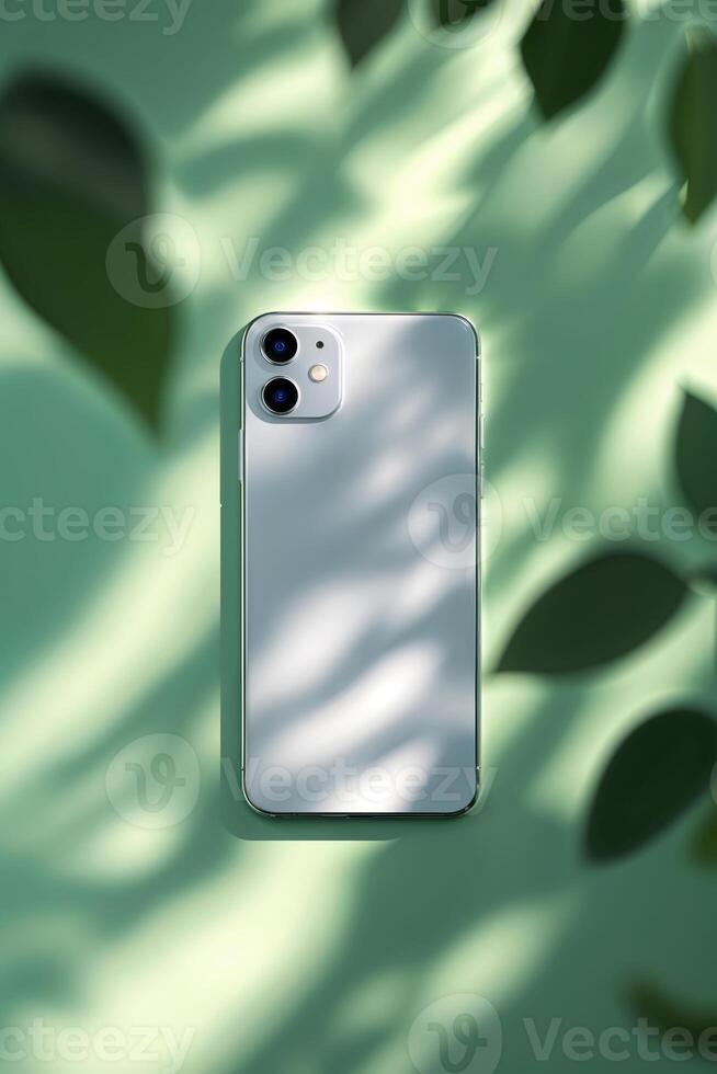 Modern smartphone resting on a green surface with soft shadows and leaves creating an aesthetic arrangement photo