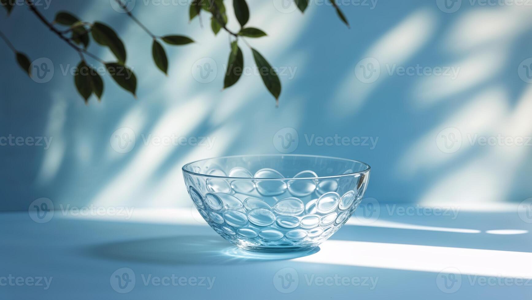 Glass bowl with circular patterns casts shadows on a blue surface illuminated by soft light from leaves photo