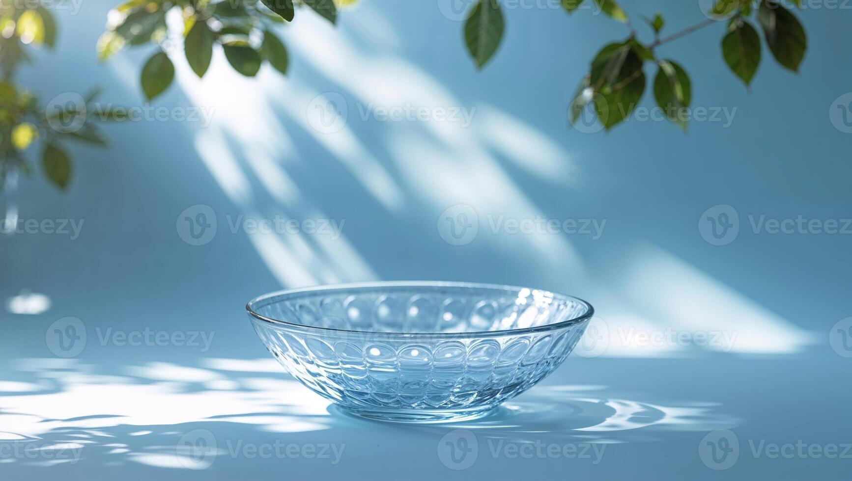 Elegant glass bowl on a soft blue backdrop with natural light casting delicate shadows from nearby leaves photo