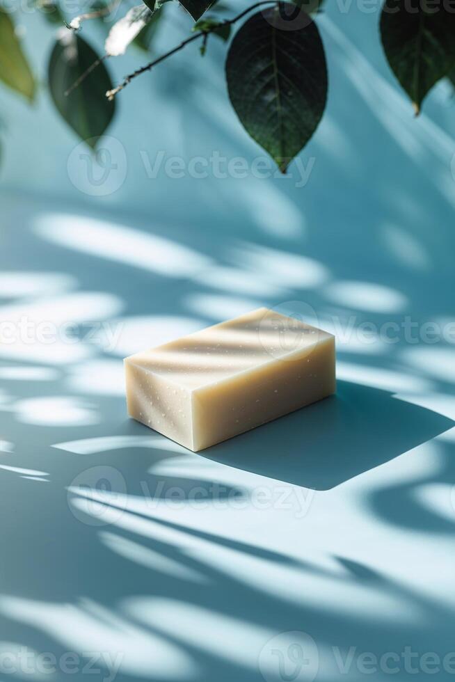 Natural handmade soap placed elegantly on a blue surface with delicate shadow patterns from green leaves photo