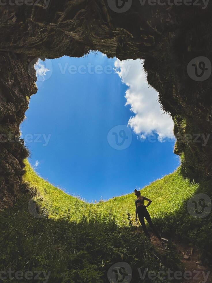 Woman Standing in Underground Cave with Hole to Outside photo