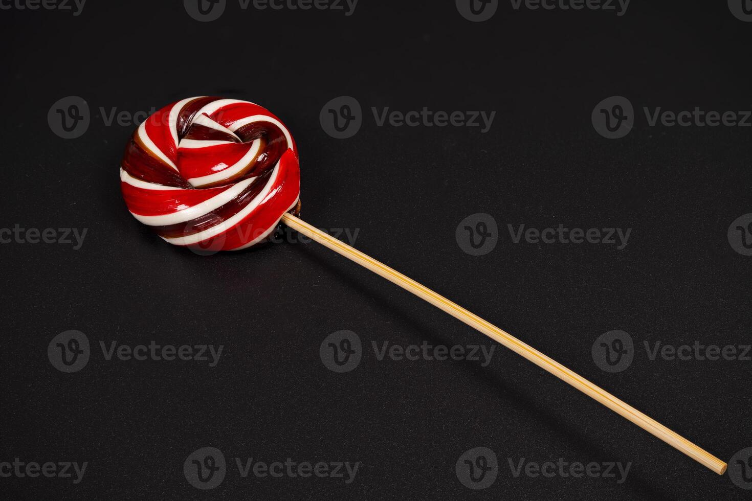 Colorful spiral lollipop on a stick against a dark background photo