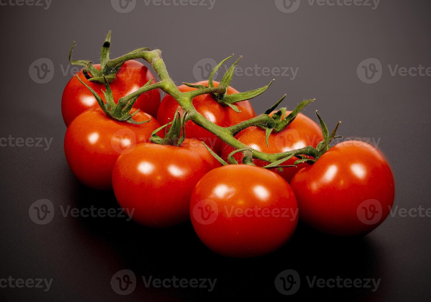 Fresh red tomatoes on a vine arranged on a dark surface photo
