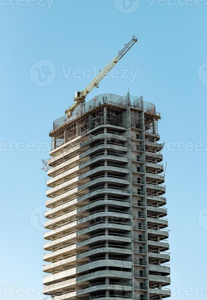 Modern architecture under construction in the city. Unfinished high-rise building with crane and photo