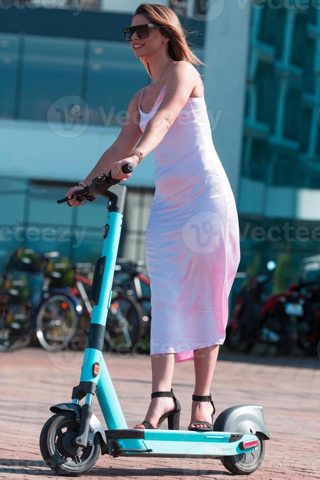 Elegant woman in a pink dress and sunglasses riding an electric scooter through the sunny city streets, embracing the freedom and style of a perfect urban adventure. photo