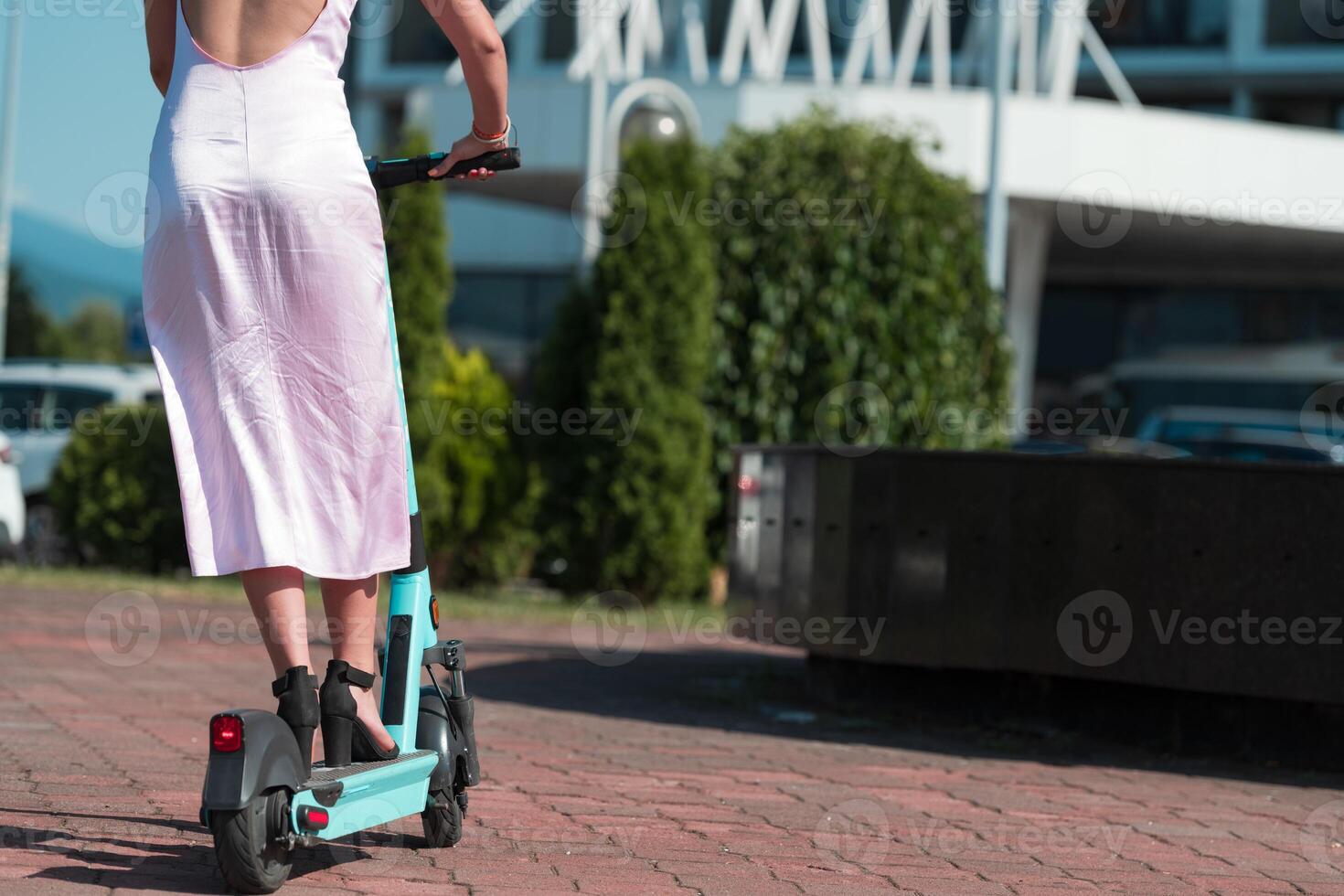 Elegant woman in a pink dress and sunglasses riding an electric scooter through the sunny city streets, embracing the freedom and style of a perfect urban adventure. photo