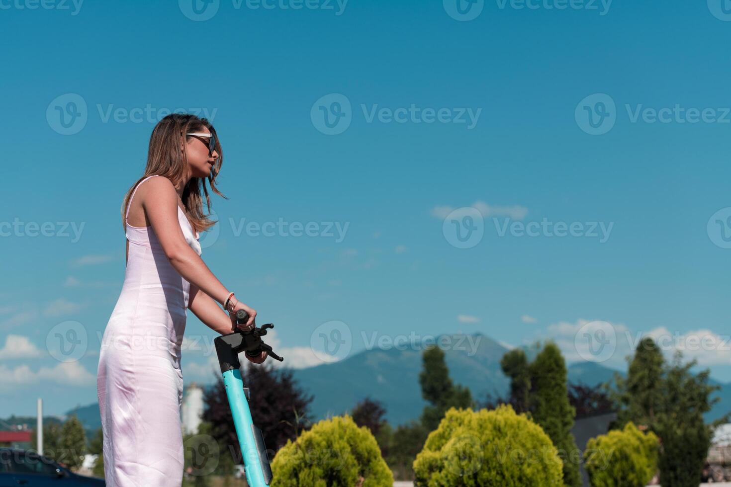Elegant woman in a pink dress and sunglasses riding an electric scooter through the sunny city streets, embracing the freedom and style of a perfect urban adventure. photo