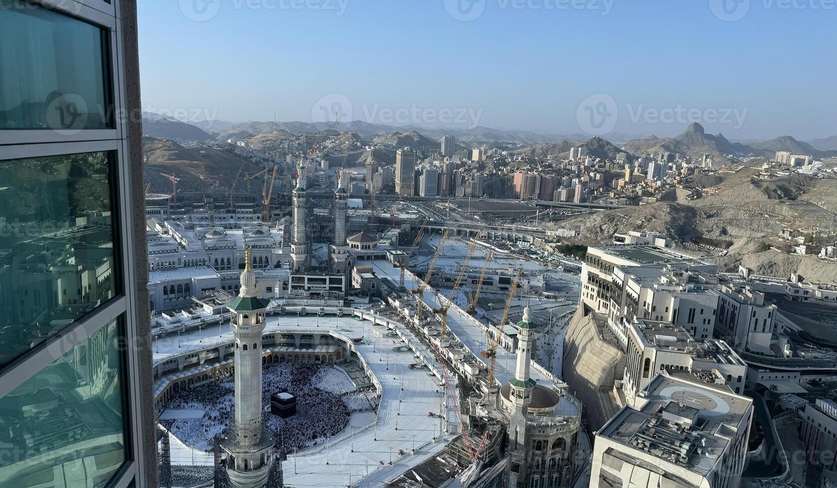 Aerial view of Masjid Al-Haram and Makkah city from the Clock Tower, Pilgrims performing Tawaf around the Kaaba during Hajj or Umrah, Magrib pray. The Holy Mosque, Minarets, and skyline highlight this photo