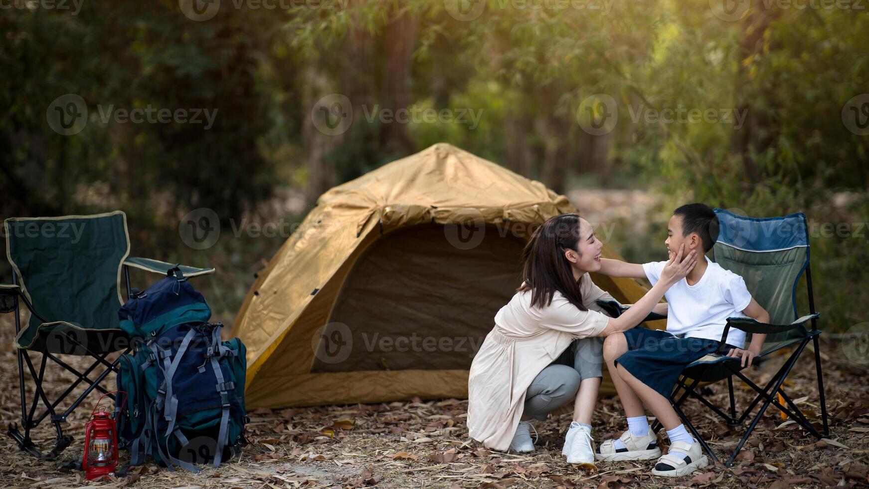 The smiling mother is touching her son face in front of the camping tent. photo