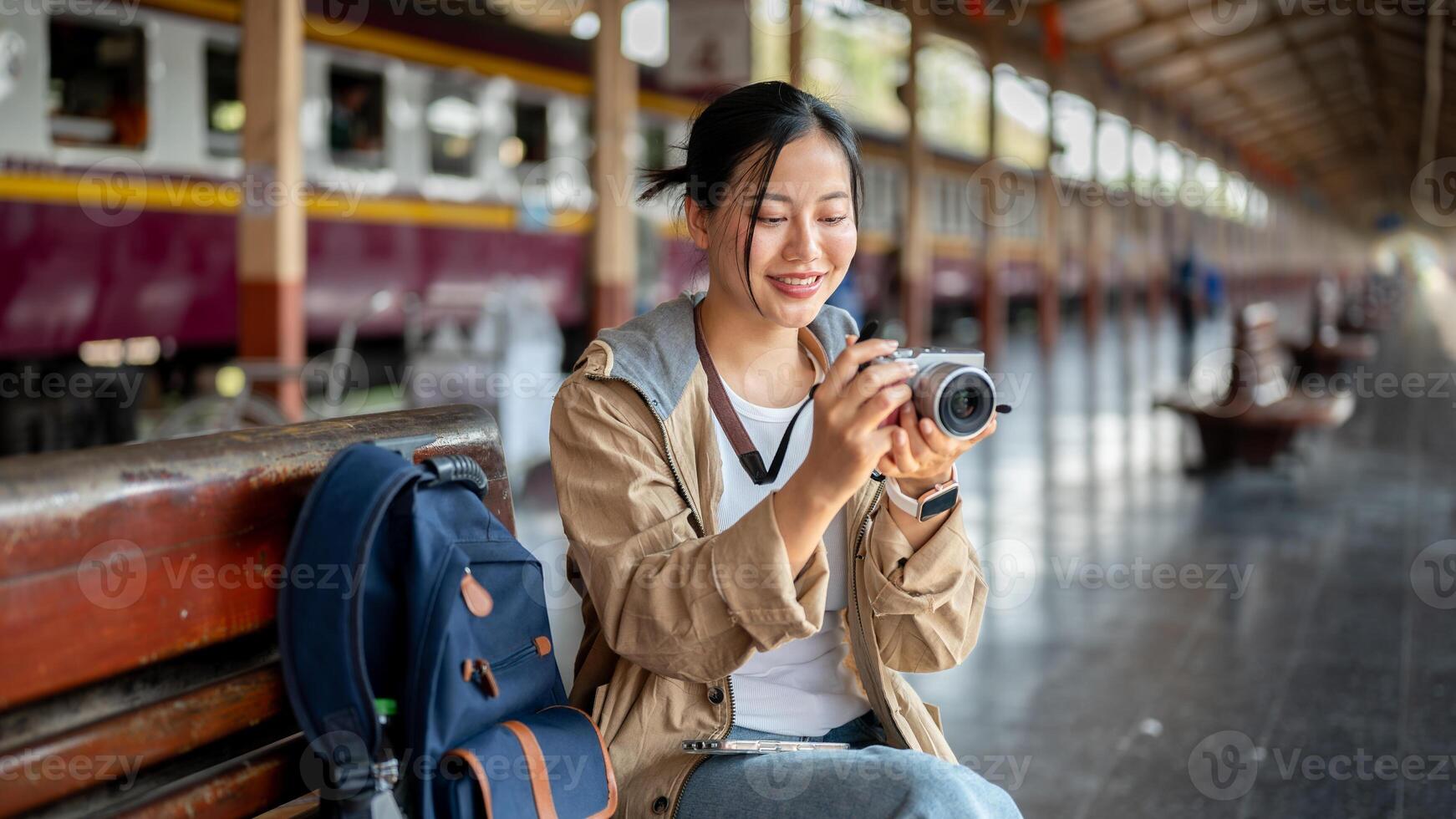 Smiling Asian woman is looking at the camera to adjust angle while sitting on the wooden benchmark. photo
