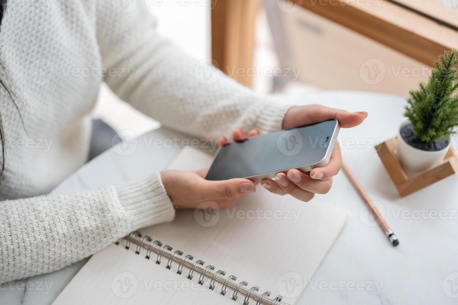 Top view of the hands holding smartphone, sitting at the round marble table with notebook and pencil photo