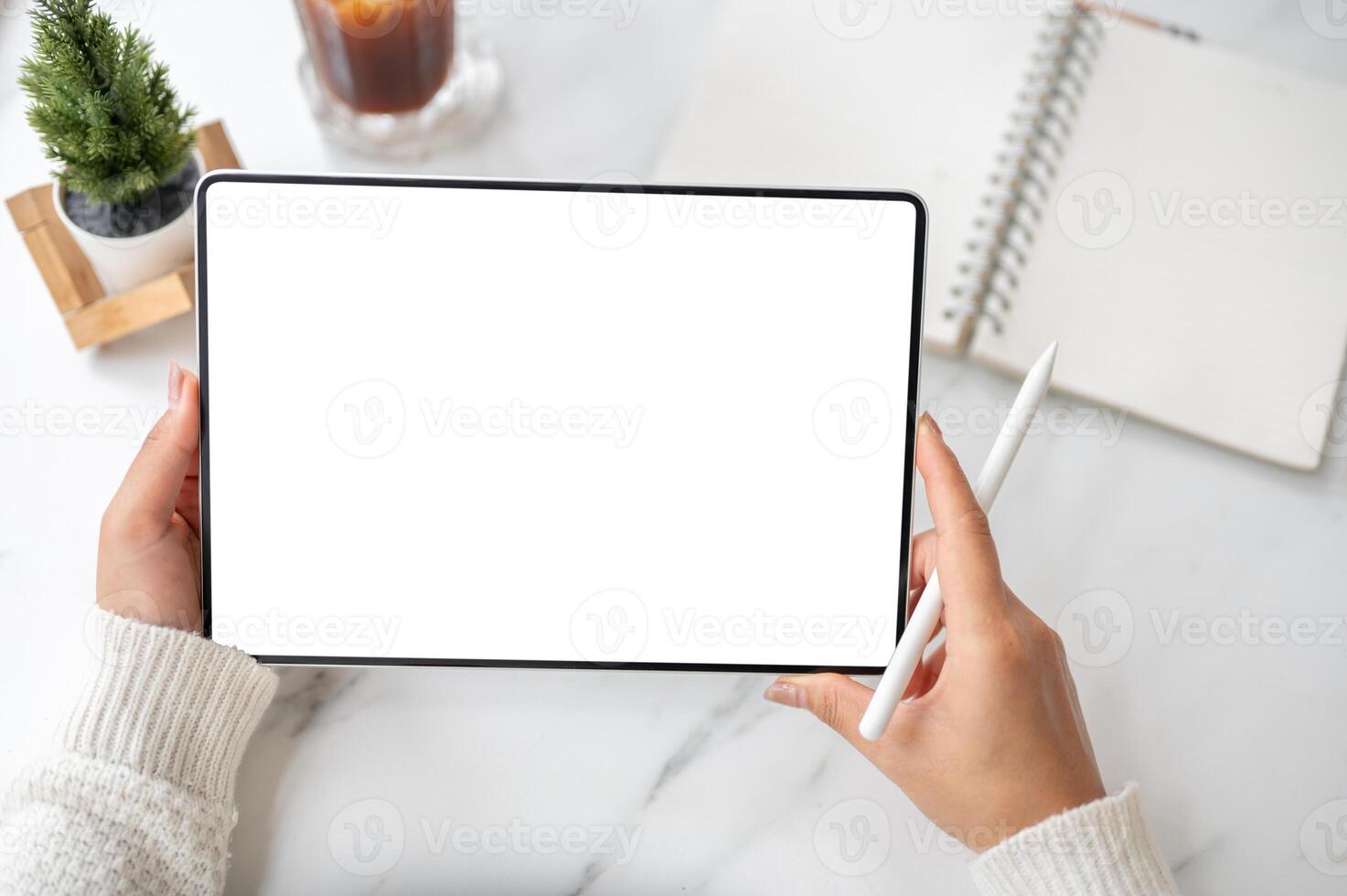 The left hand holding blank screen tablet horizontally with stylus pencil in right hand on the table photo