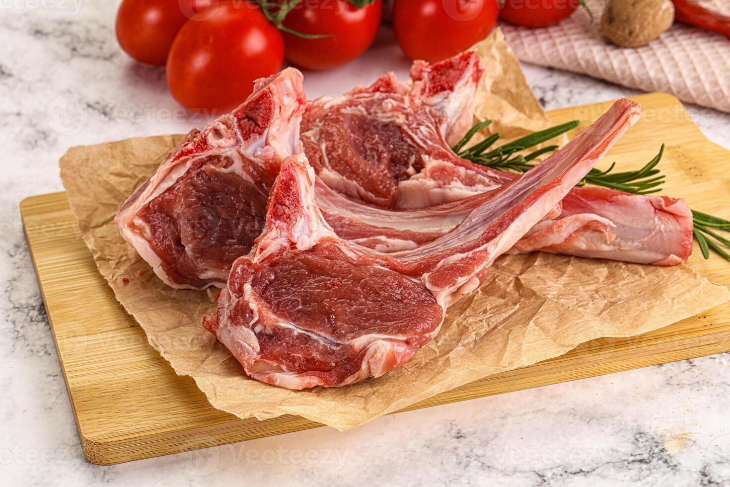 Raw lamb chops on a cutting board with tomatoes photo