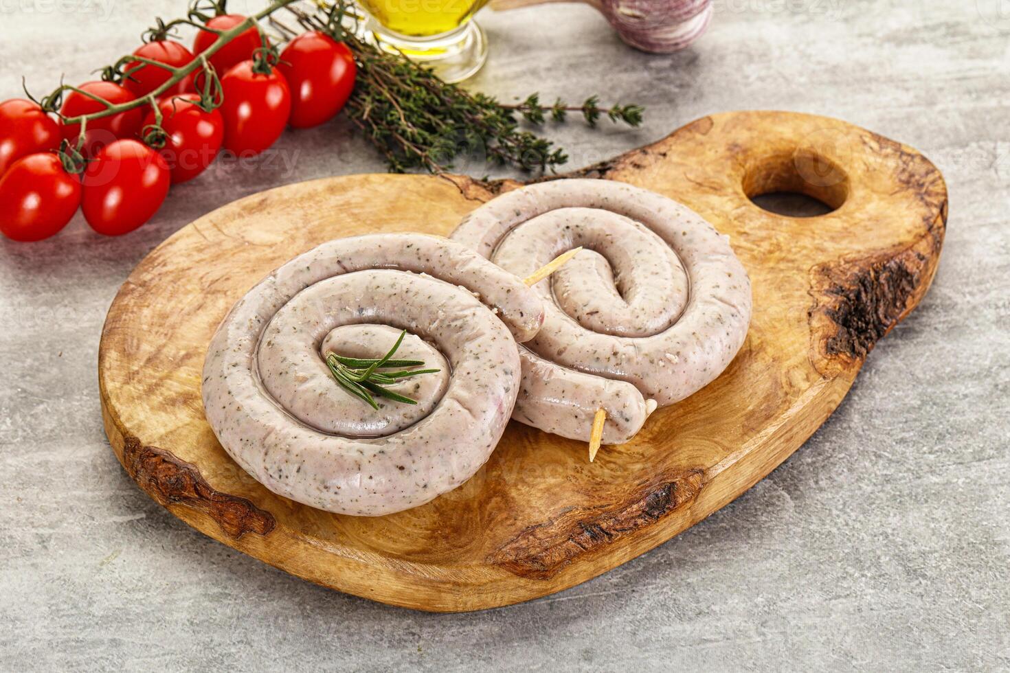 Two sausages on a wooden cutting board with tomatoes and herbs photo