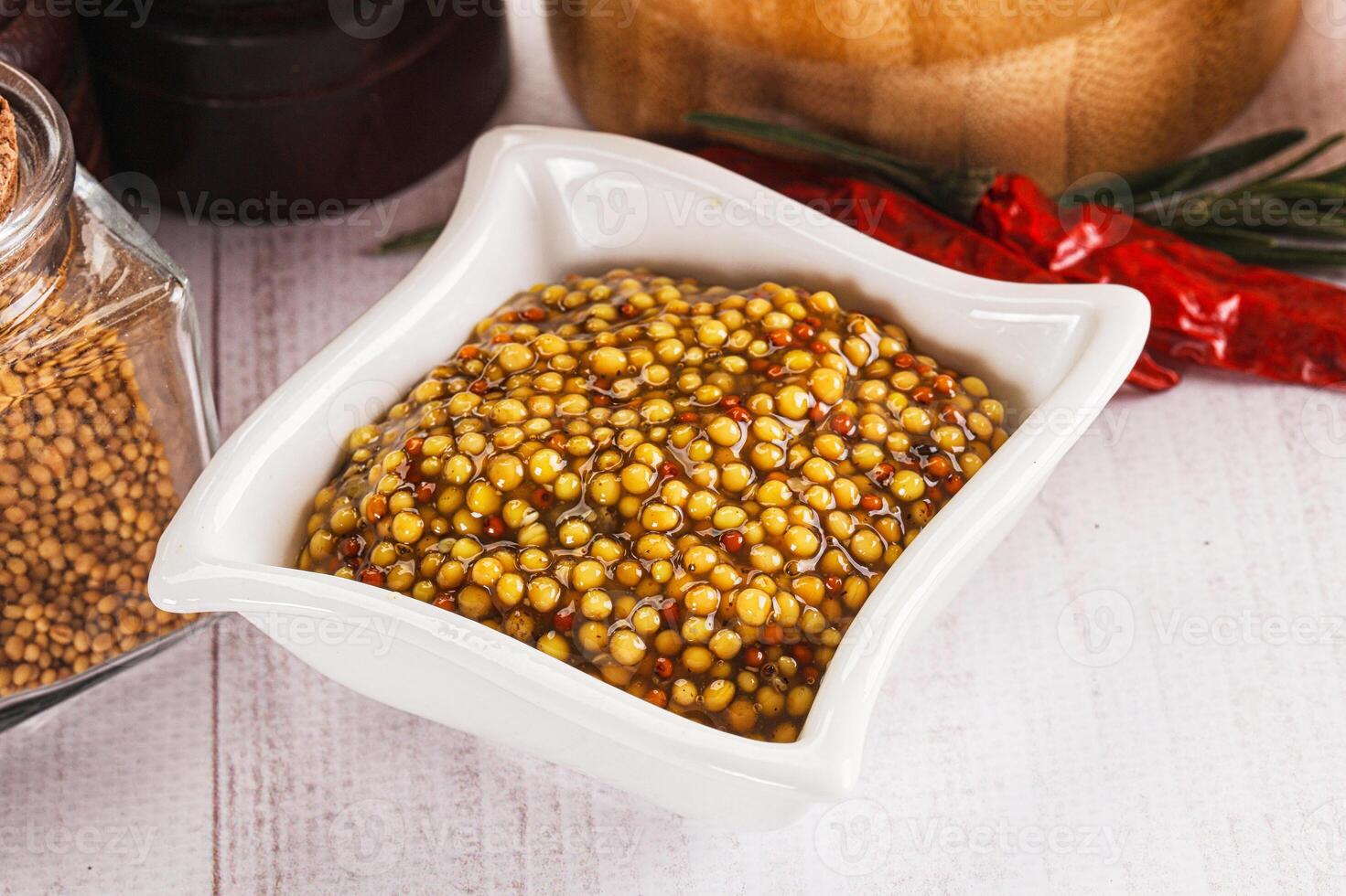 A bowl of mustard next to a jar of chili powder photo