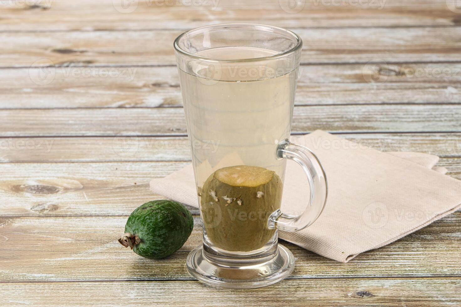 A glass of water and a green fruit on a table photo
