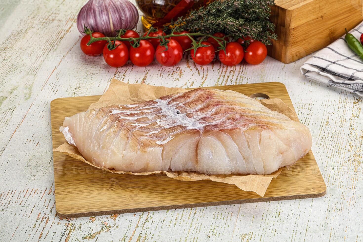 A piece of fish on a cutting board with vegetables and spices photo