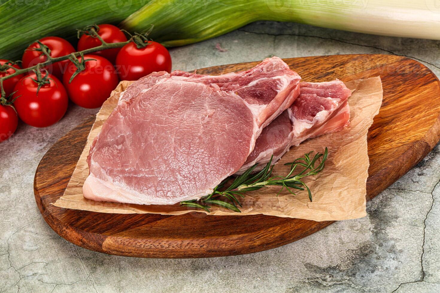Raw pork on a wooden cutting board with tomatoes and herbs photo