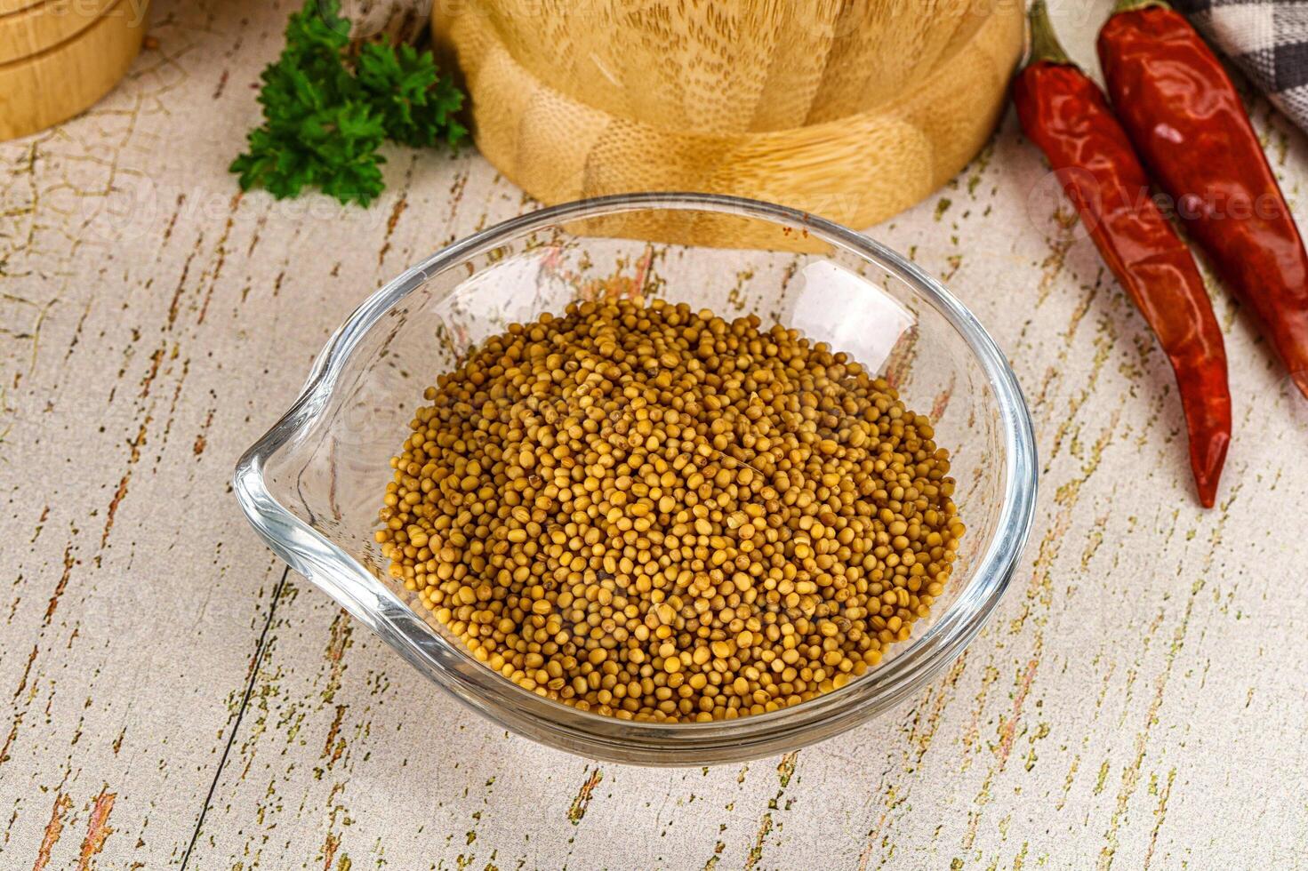 A bowl of mustard seeds and a wooden spoon on a wooden table photo
