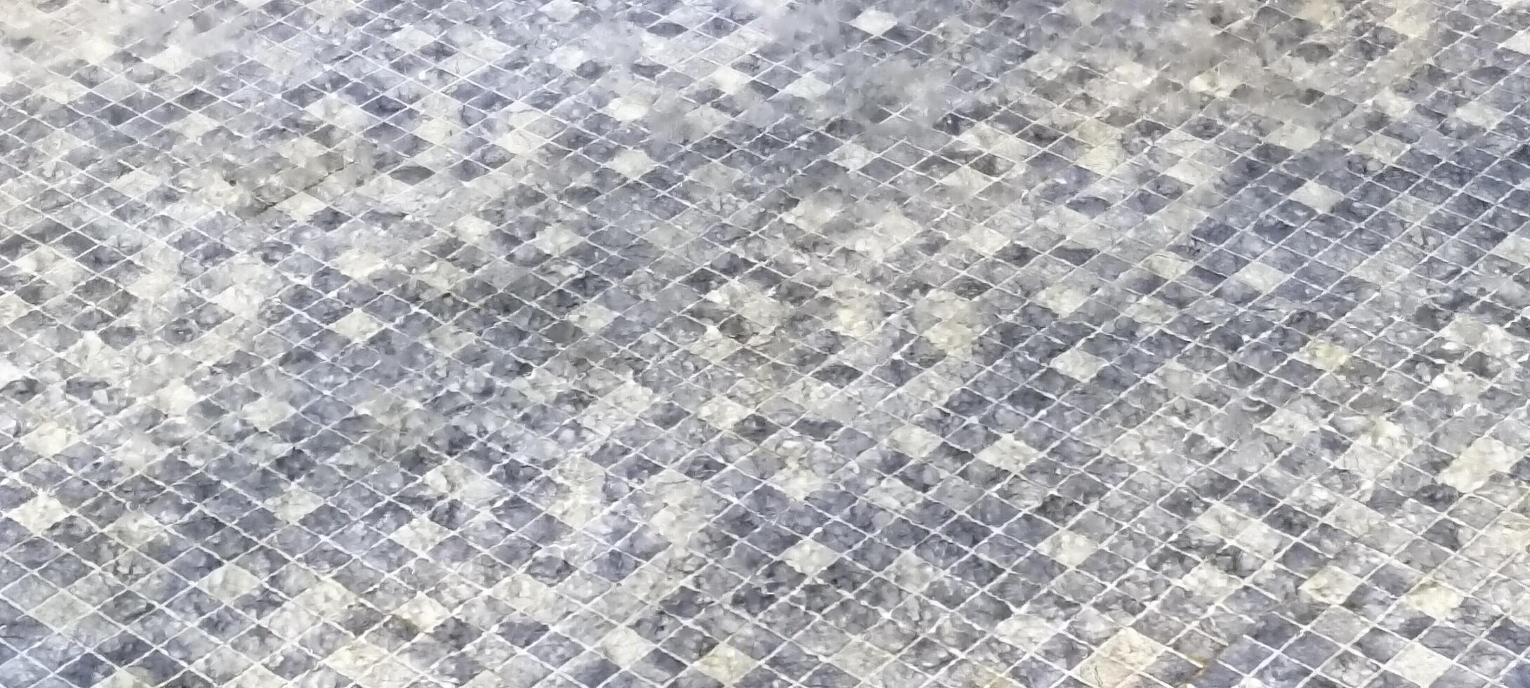 A detailed view of a mosaic-tiled floor covered in water droplets, creating a textured and reflective surface. The small square tiles display various shades of gray, adding depth to the design. photo