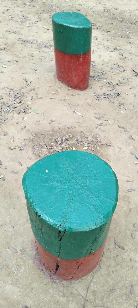 Two wooden stumps, painted half green and half red, stand on dry, leaf-covered ground. The texture of the wood is visible through the paint, giving them a rustic yet artistic appearance. photo
