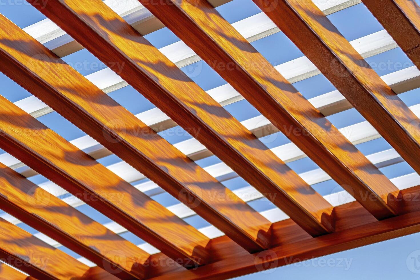 Bright Light and Shadow Play on a Wooden Pergola Structure Against a Clear Blue Sky photo