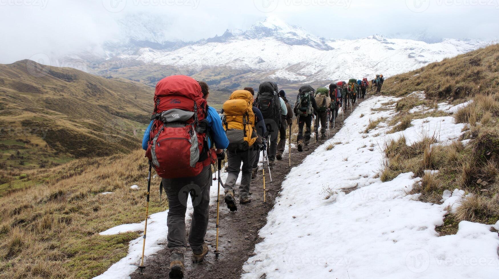 A group of hikers make their way along a snowy trail in the Andes Mountains. The landscape features rolling hills and distant peaks, with cloudy skies overhead photo