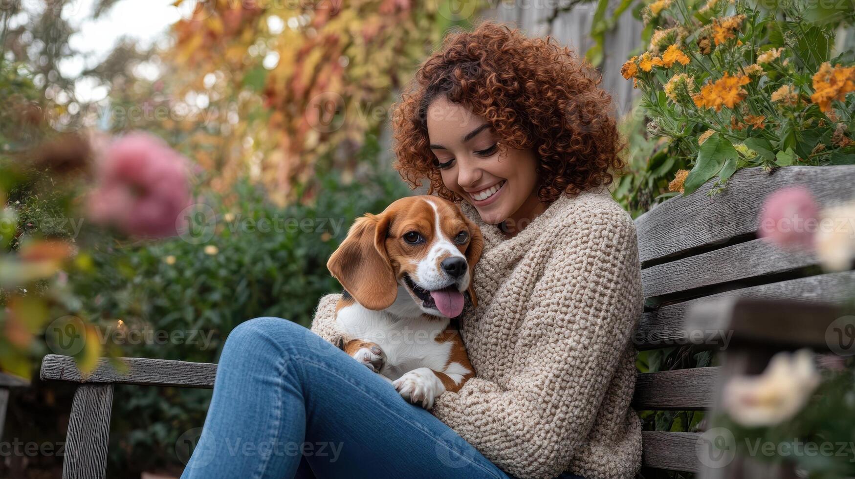 Smiling young woman with curly hair hugging beagle dog on wooden bench in garden photo