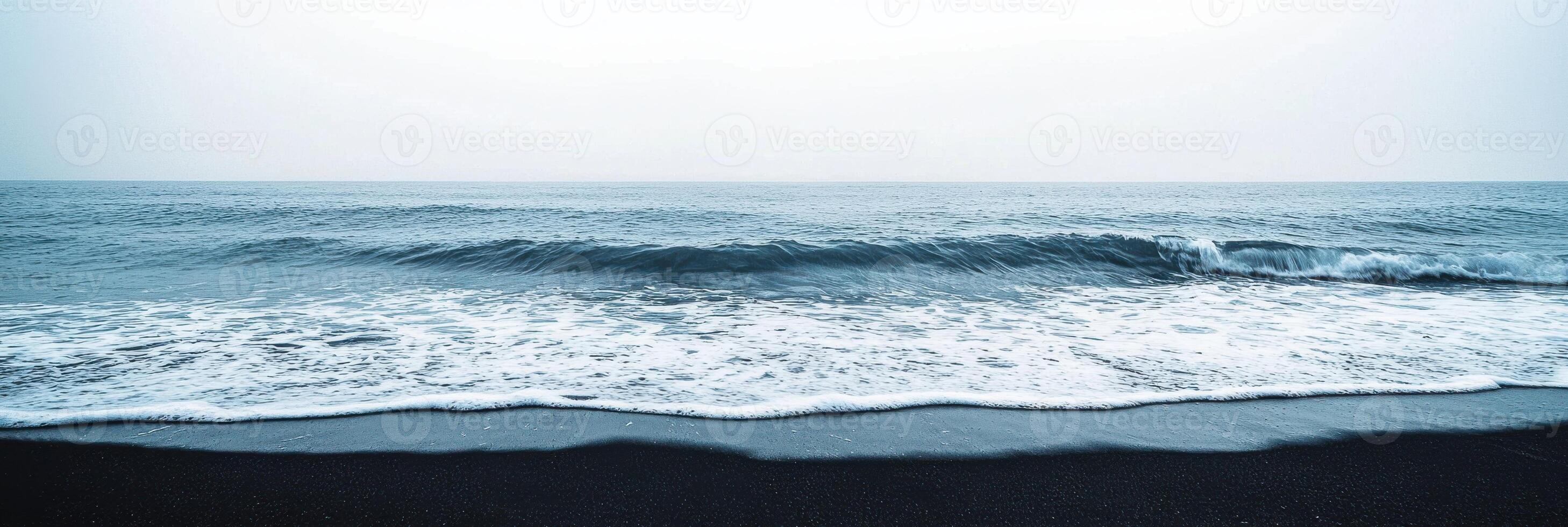 Serene view of ocean waves hitting the black sand beach on overcast day photo