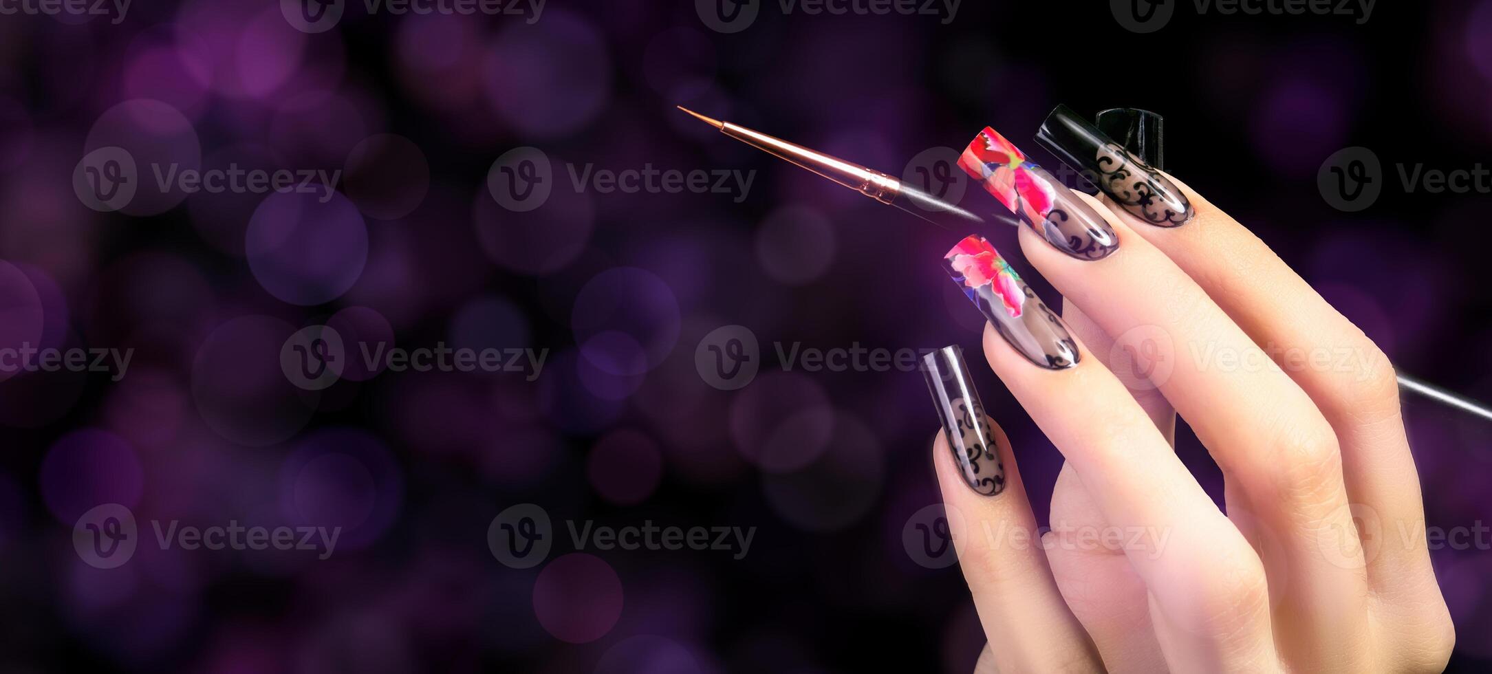 A hand with a beautiful manicure and a brush on a black background with purple bokeh spots. Nail design. Extended nails. photo