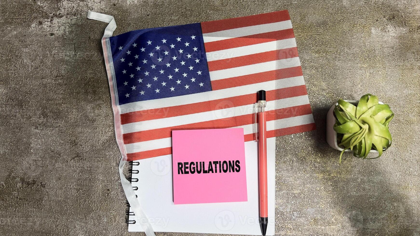 Concept of Regulations write on sticky notes and Flag of the United States isolated on Wooden Table. photo