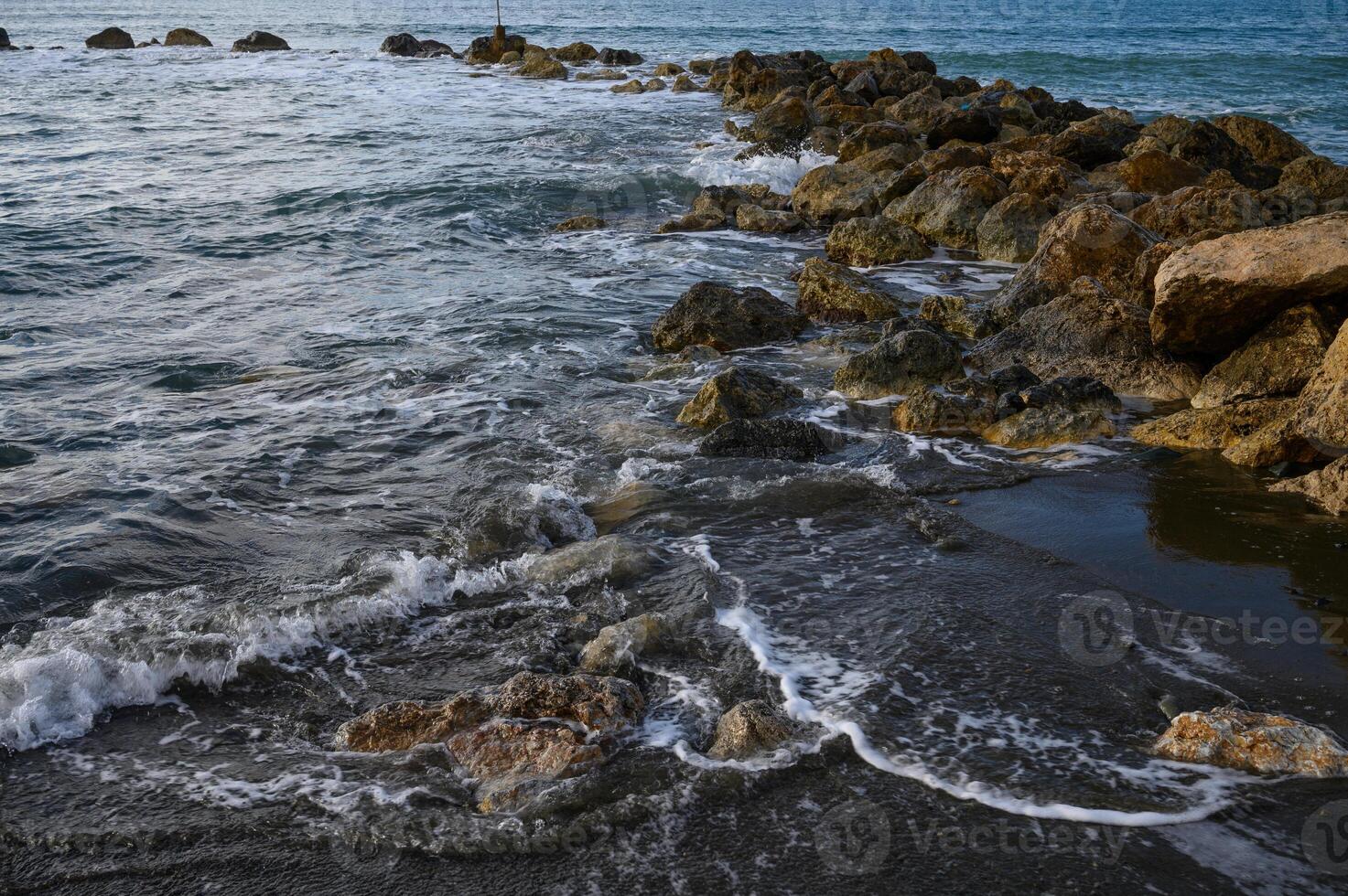 Waves gently lap against rocky shore at sunset with vibrant colors and serene atmosphere photo