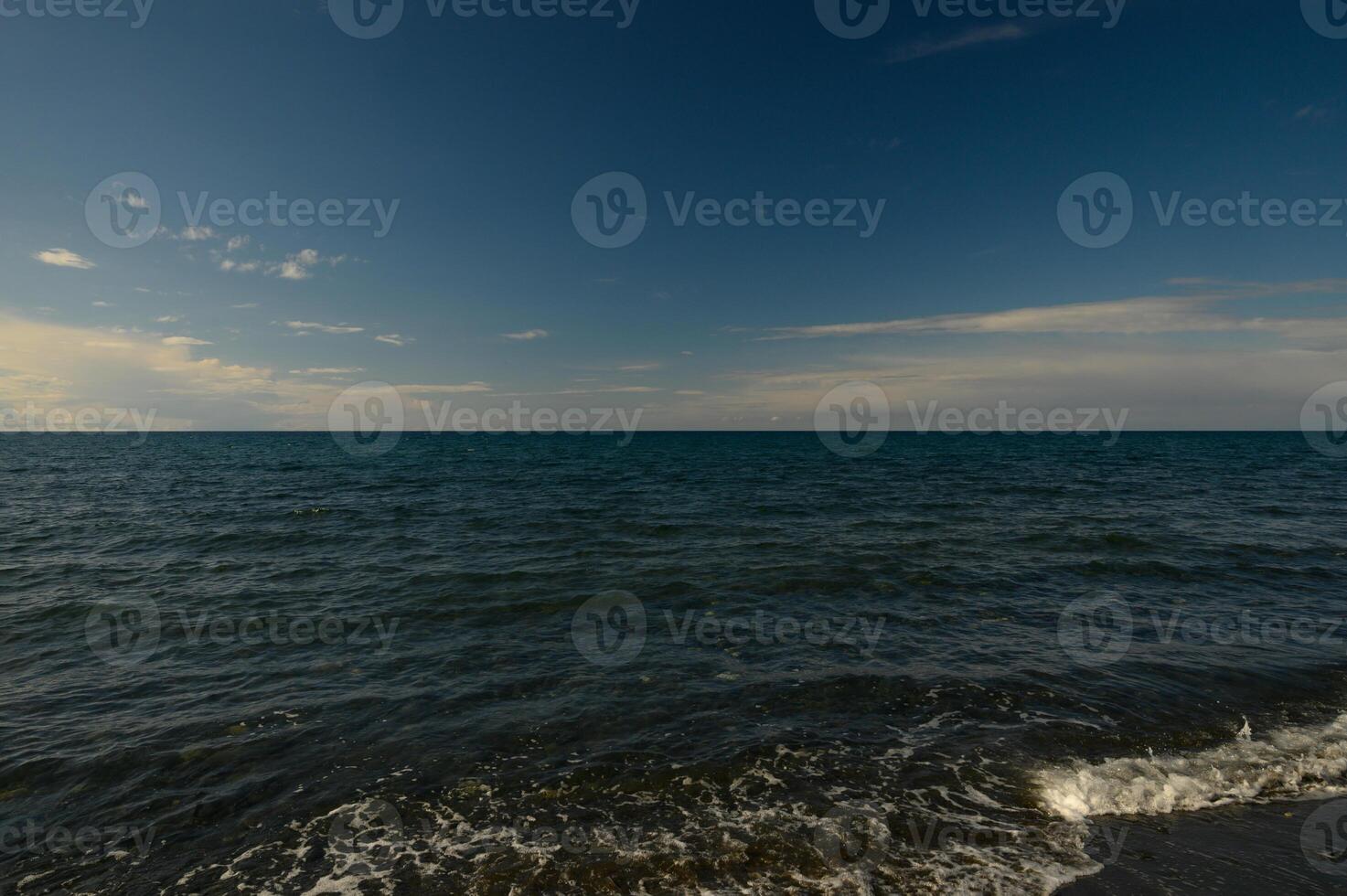 Calm waters stretch endlessly under a serene sky at the beach during golden hour in late afternoon photo