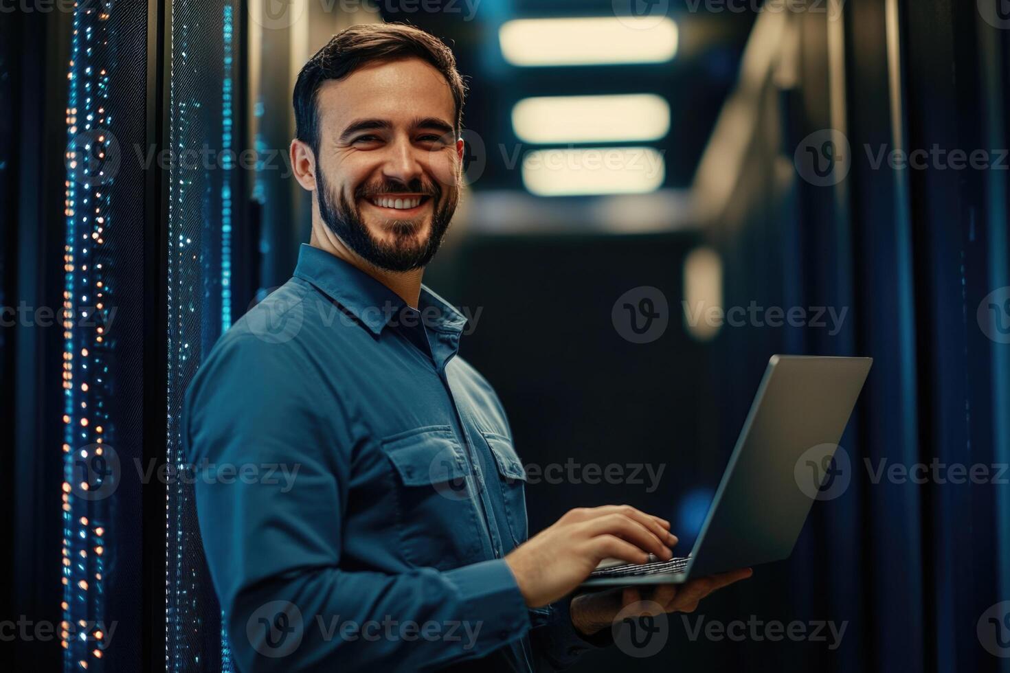 A smiling man in a server room holding a laptop photo