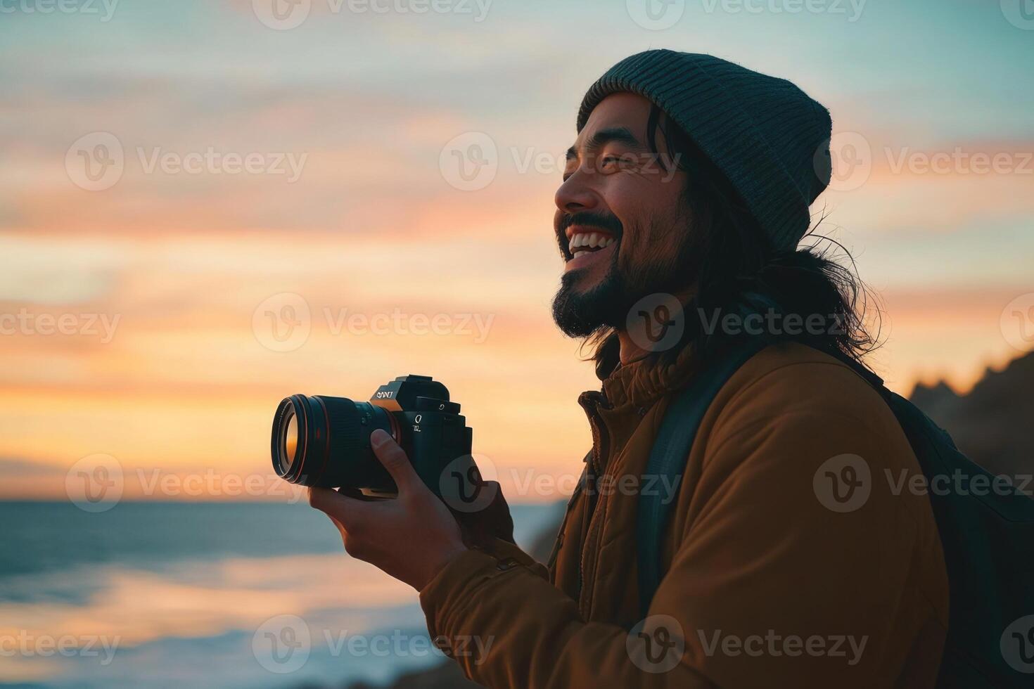A man with a backpack and a camera smiles while looking at the ocean photo