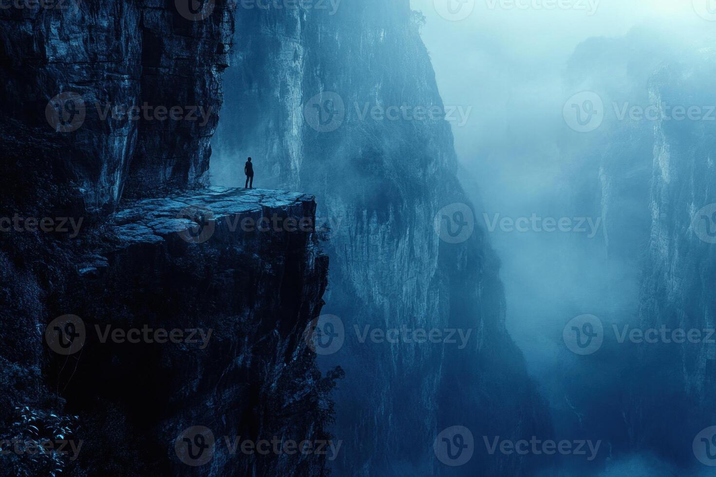 A lone person standing on a cliff in the middle of a mountain photo