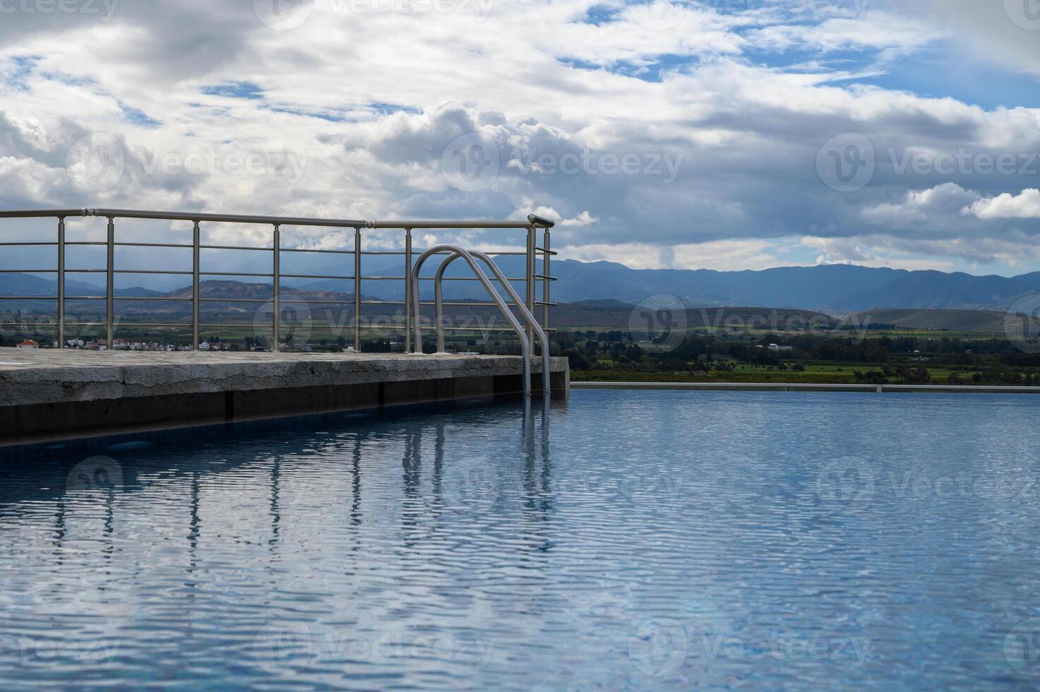 Serene infinity pool overlooking lush valleys and majestic mountains under a cloudy sky photo
