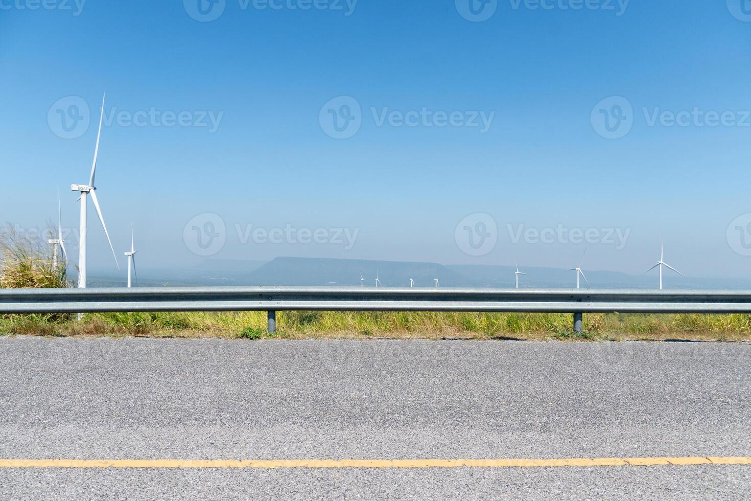Horizontal view asphalt road with guard lens. Wind turbines tower over a lush forest. photo
