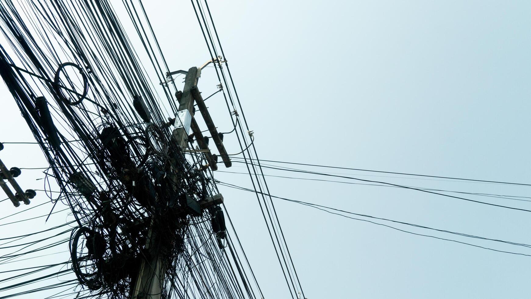Different communication cables are attached to concrete poles. The chaos of unorganized cable installation in Thailand. under view of clear sky. photo