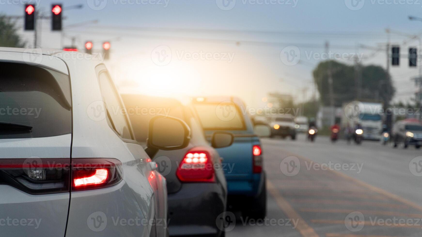 Line of cars stopped at a traffic light during daylight. Cars are in focus with a blurred background of more vehicles and traffic lights suggesting a busy intersection. photo