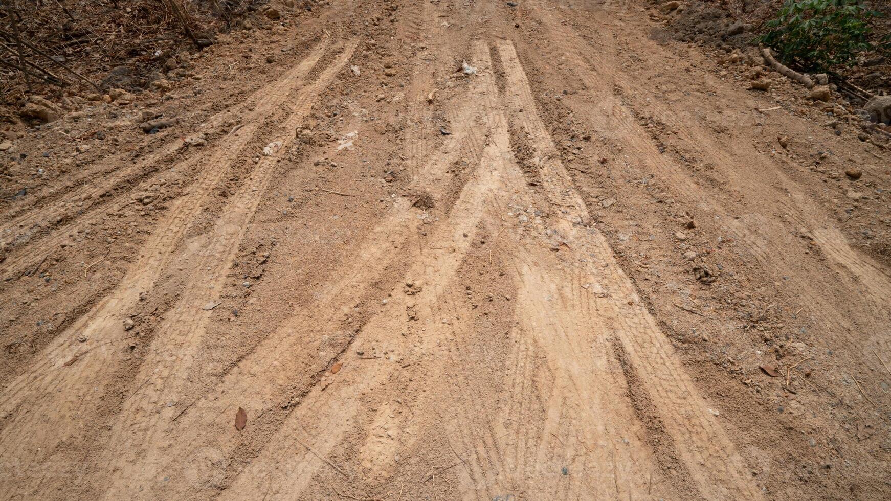Dirt road or path with visible tire tracks indicating vehicle passage. The ground is rough and textured with a mix of light and dark soil suggesting a rural or unpaved setting. photo