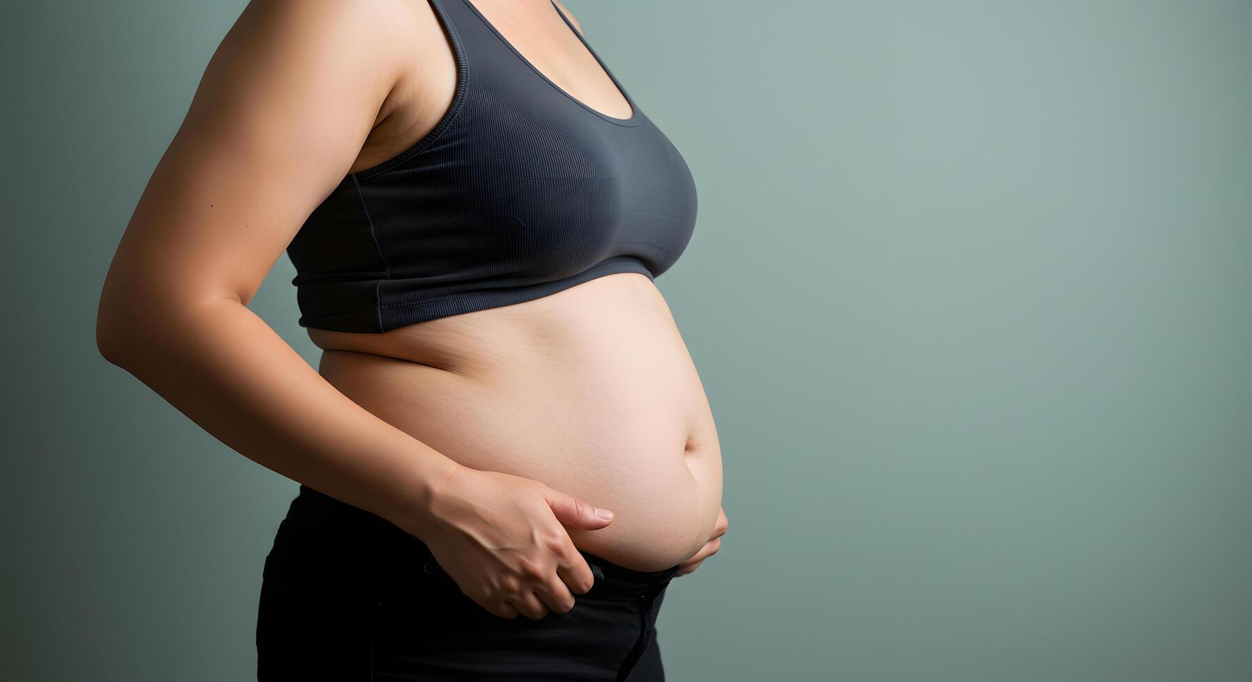 A Side Profile of an Overweight Woman Wearing a Sports Bra and Black Pants Against a Teal Background photo