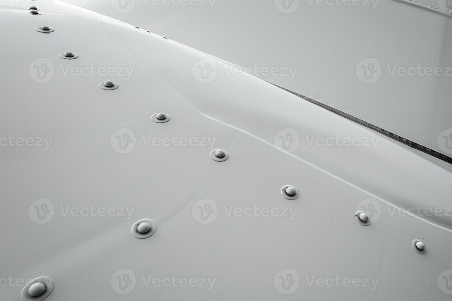 Close-up view of textured aluminum tail with rivets against smooth matte white paint surface photo