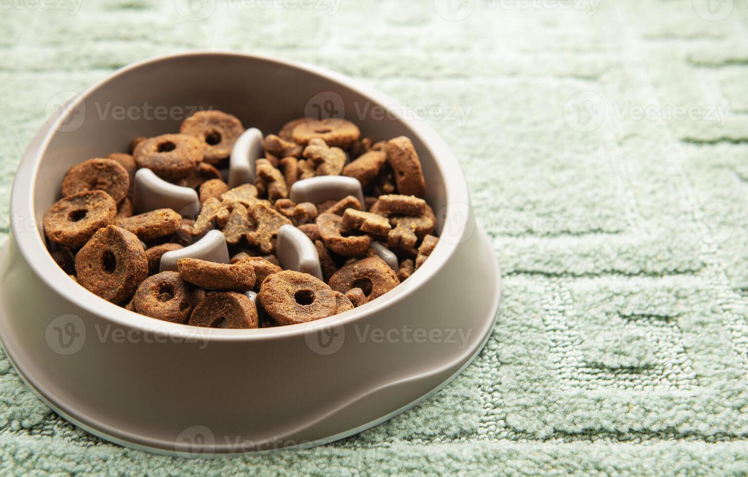 Slow feeder bowl filled with dog kibble on textured green surface photo