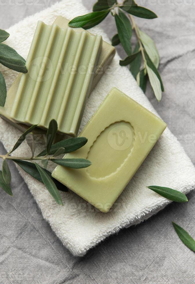 Natural olive soap bars resting on soft white towel with fresh olive branches photo