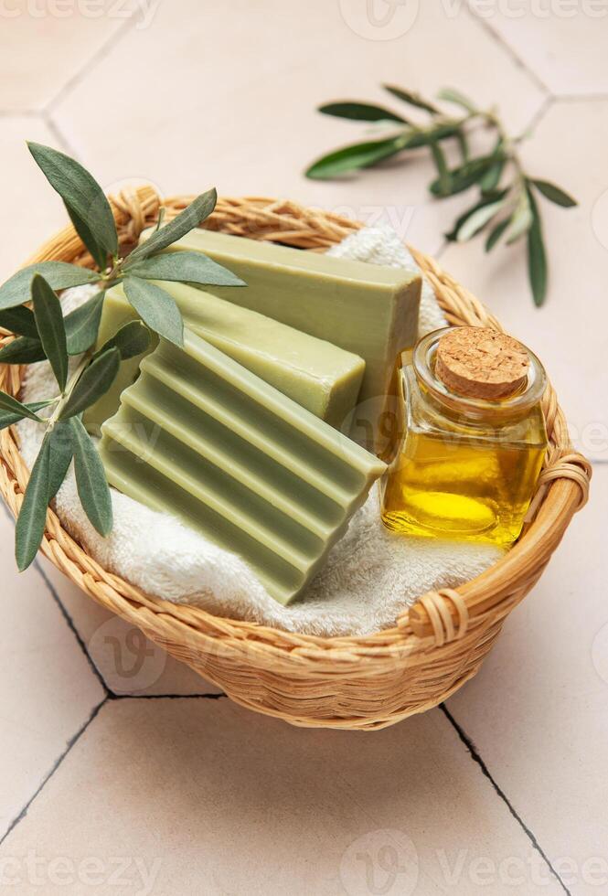 Olive soap, olive oil and branches resting in wicker basket on beige tile photo