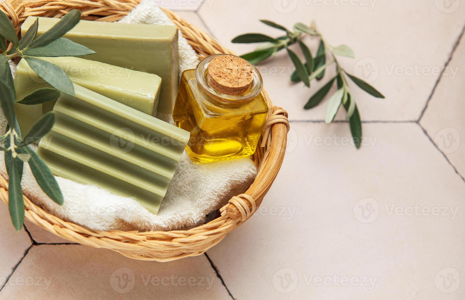 Olive soap bars, olive oil and branches resting in wicker basket on beige tile photo