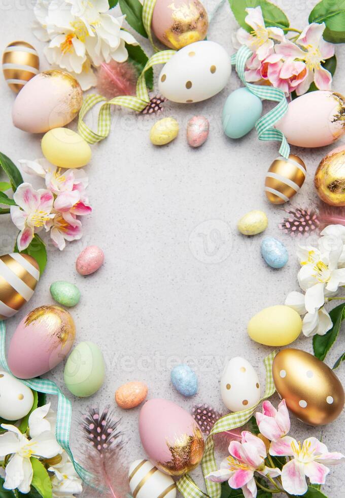 Easter eggs frame on a gray concrete background with flowers and feathers photo